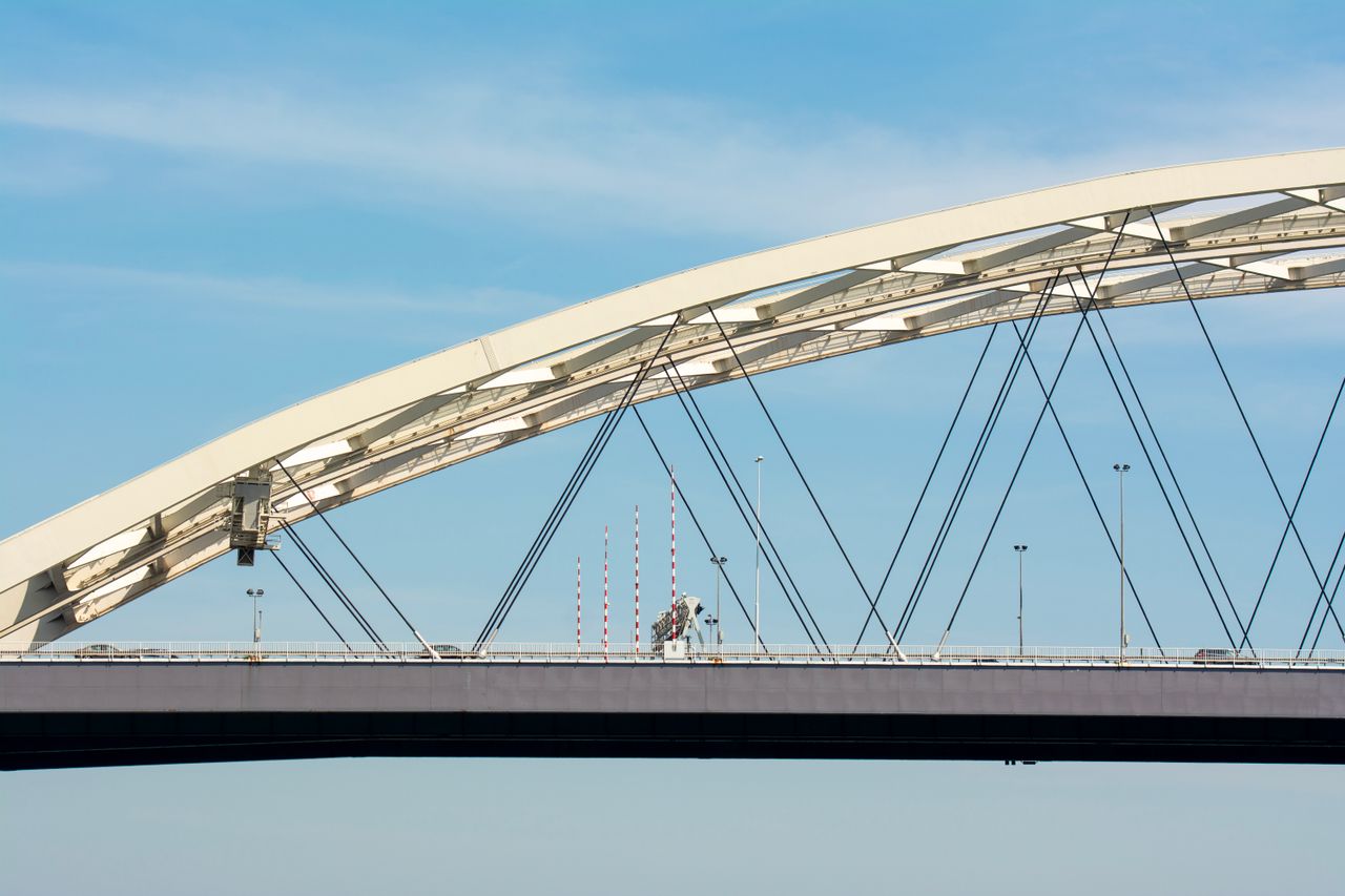 Modern arch bridge spanning under a clear blue sky in Rotterdam, Netherlands.